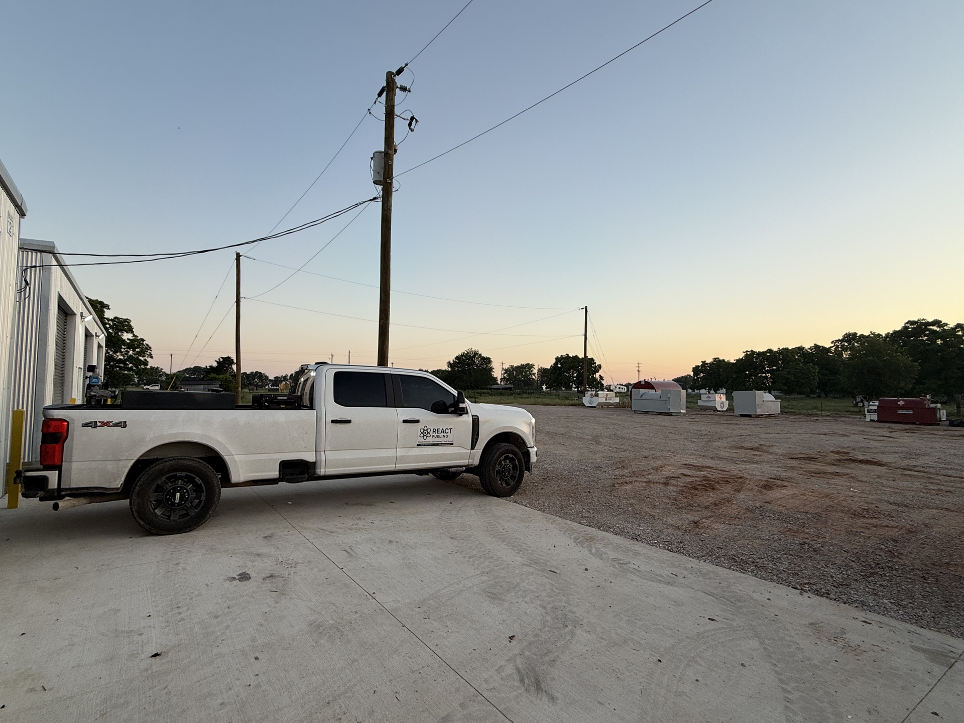 White pickup truck parked on a gravel lot at sunset with utility poles and buildings in the background