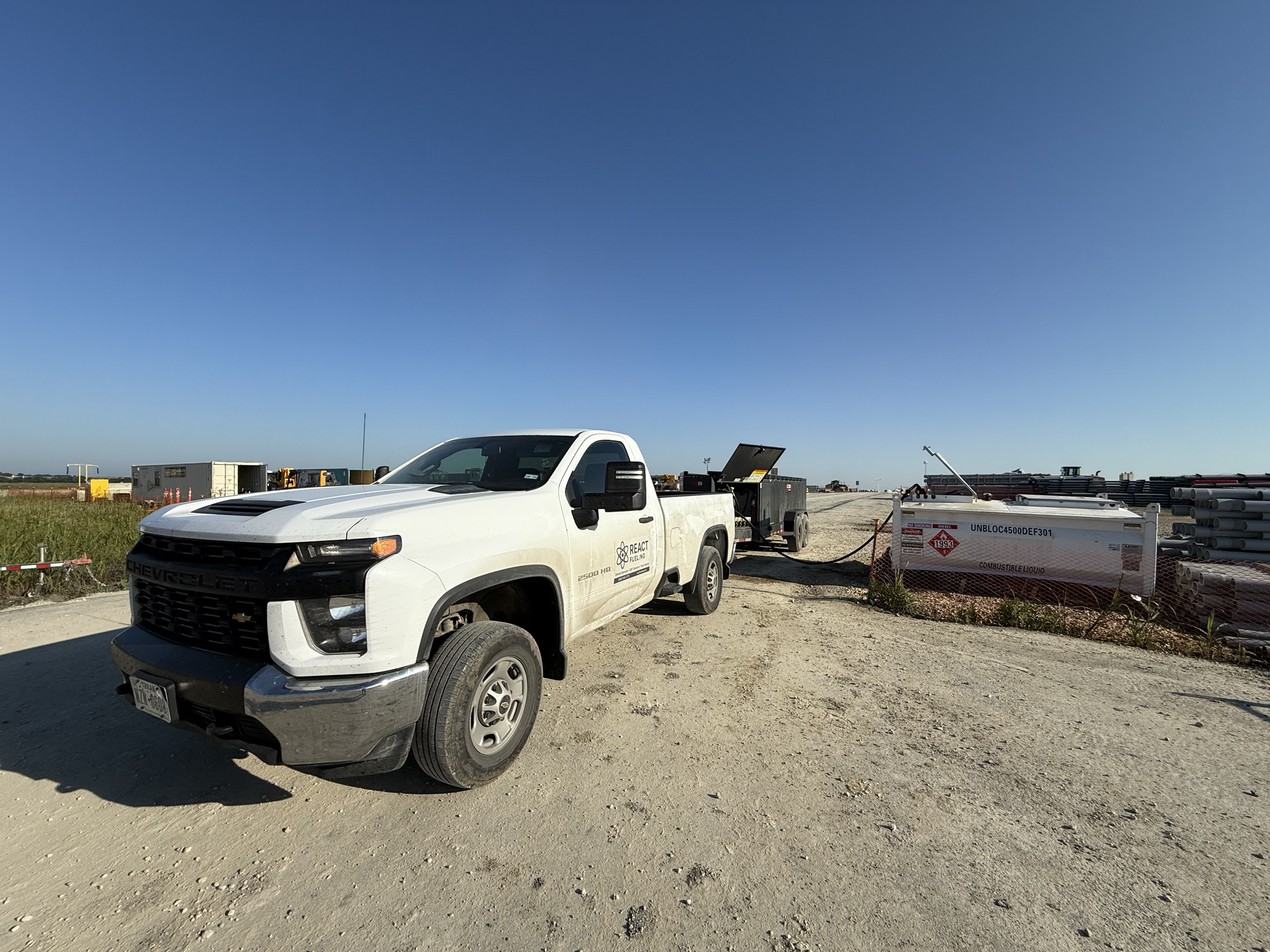 White pickup truck on a gravel lot beside farm equipment under a clear blue sky