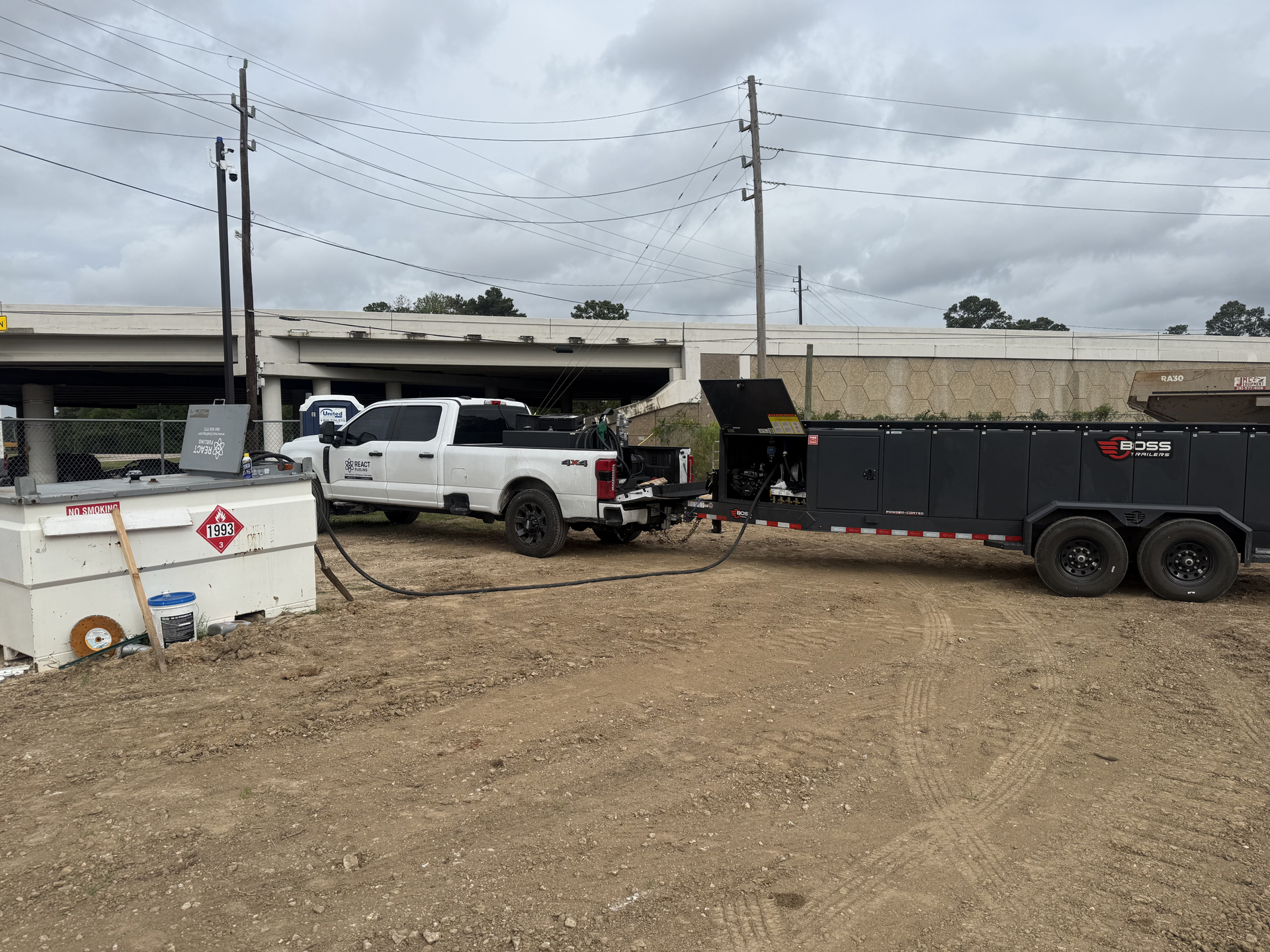 White pickup and black dump trailer at a dirt construction site under cloudy skies