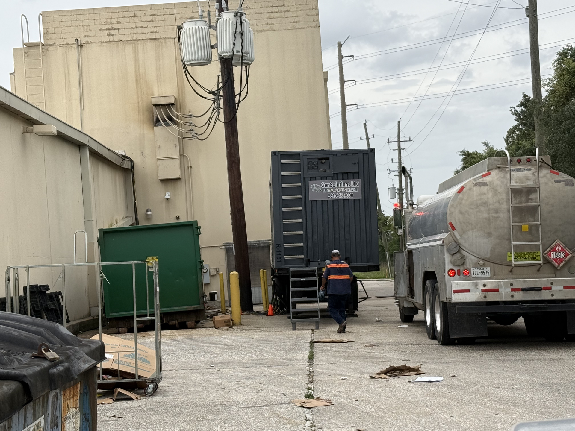 Industrial alley with a truck, dumpster, utility poles, and a worker walking away near a loading dock