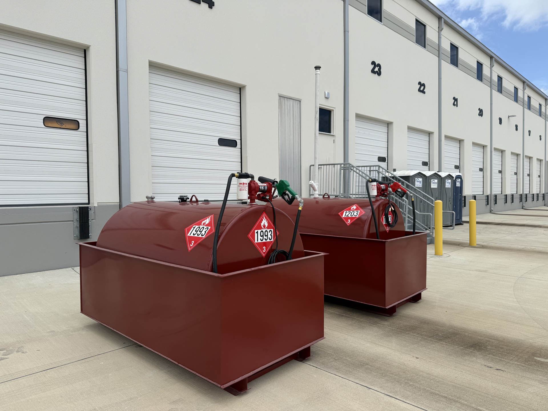 Two red industrial dumpsters beside a warehouse loading dock with closed roll-up doors