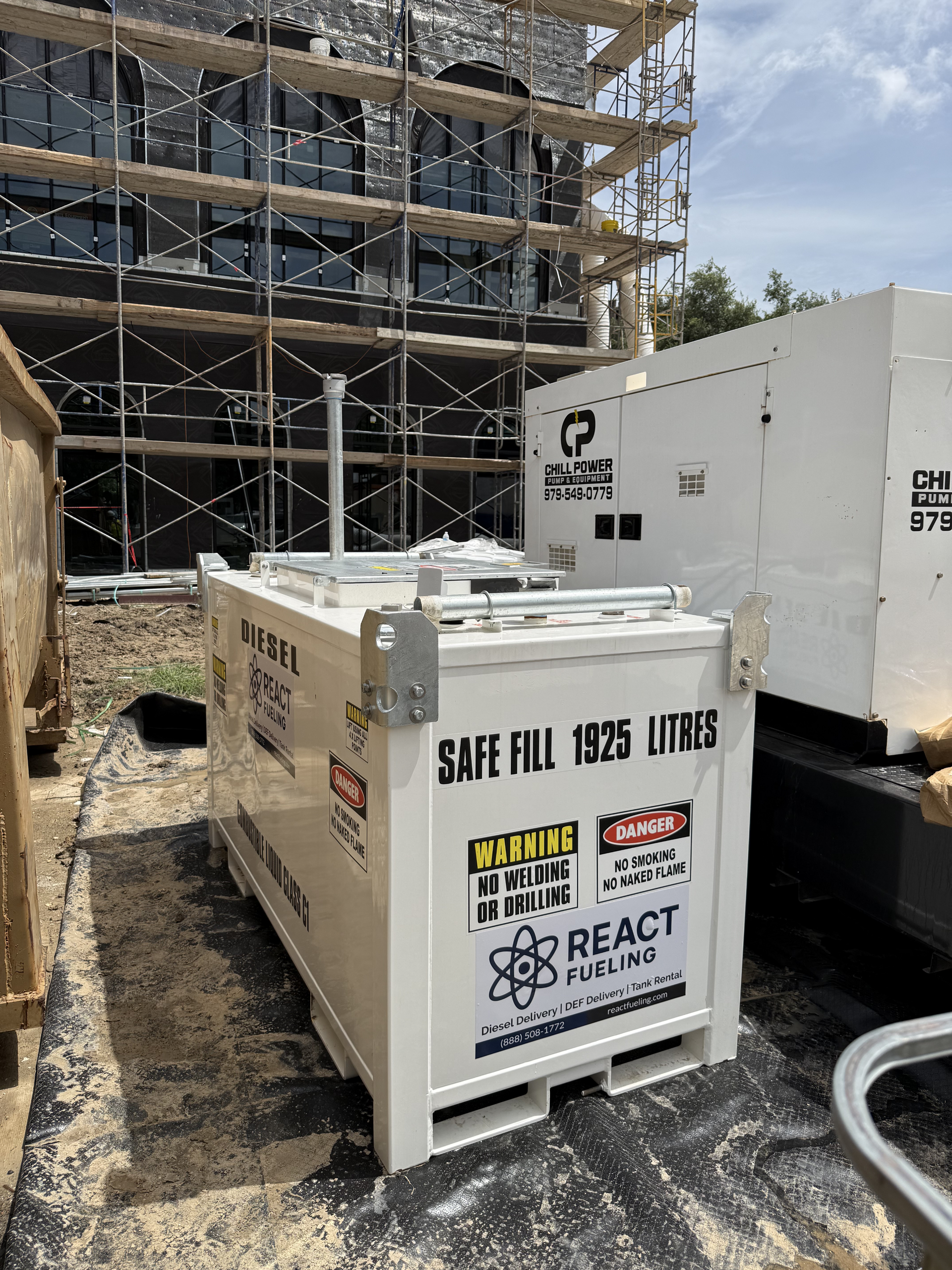 White utility dumpsters at a construction site beside scaffolding and a partially built brick building.