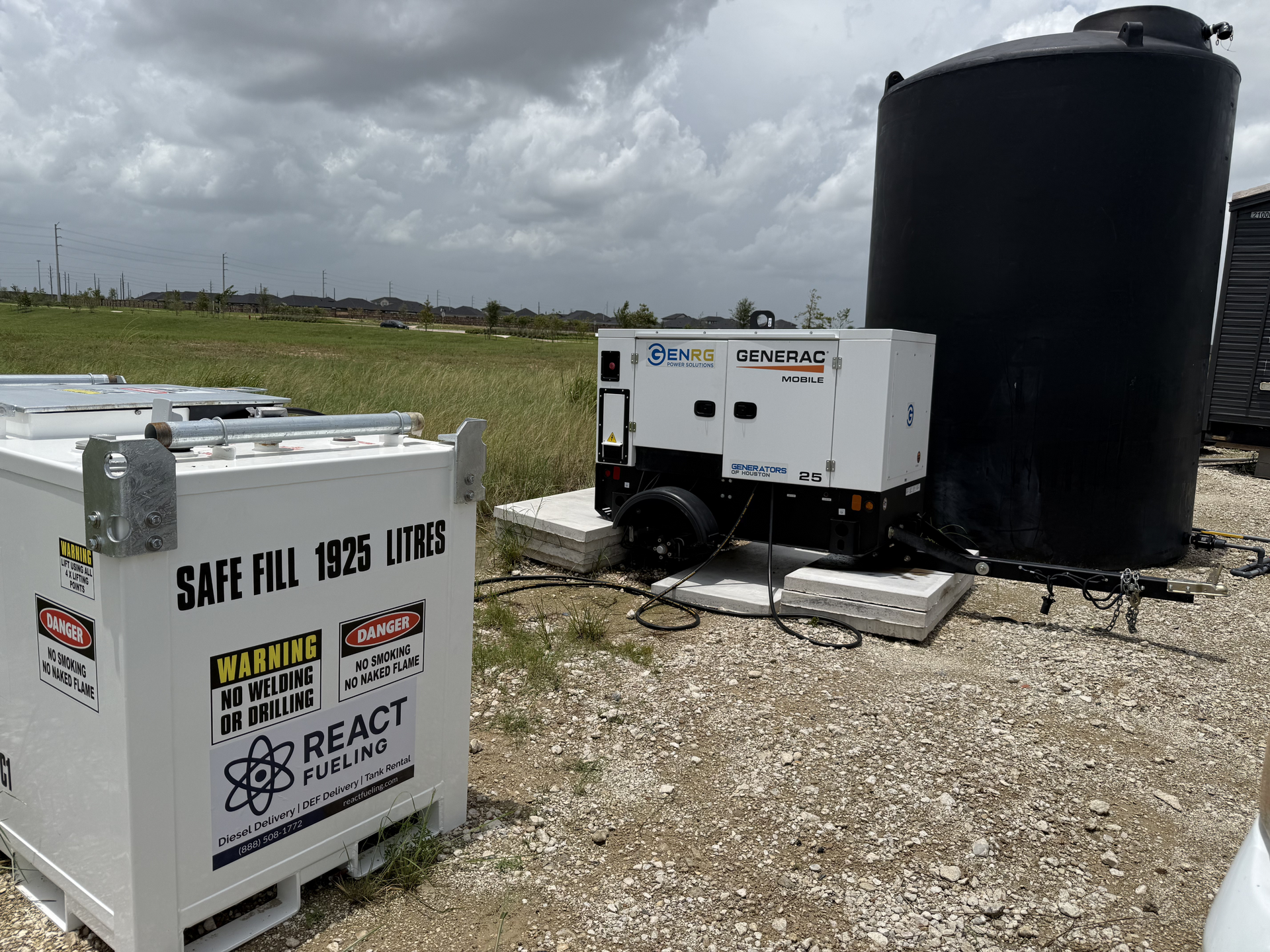 Hazardous waste storage area with black tank, generator, and white safety container in a gravel field