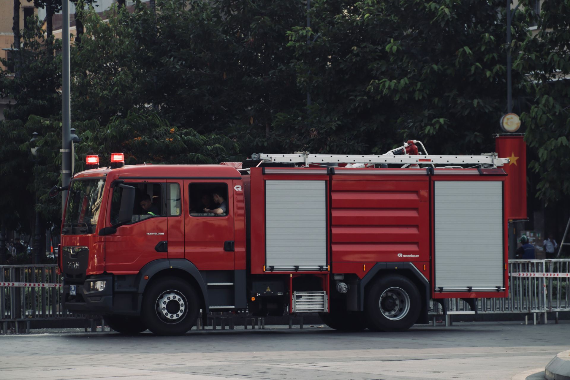 Red fire truck parked on a street beside a fence and trees