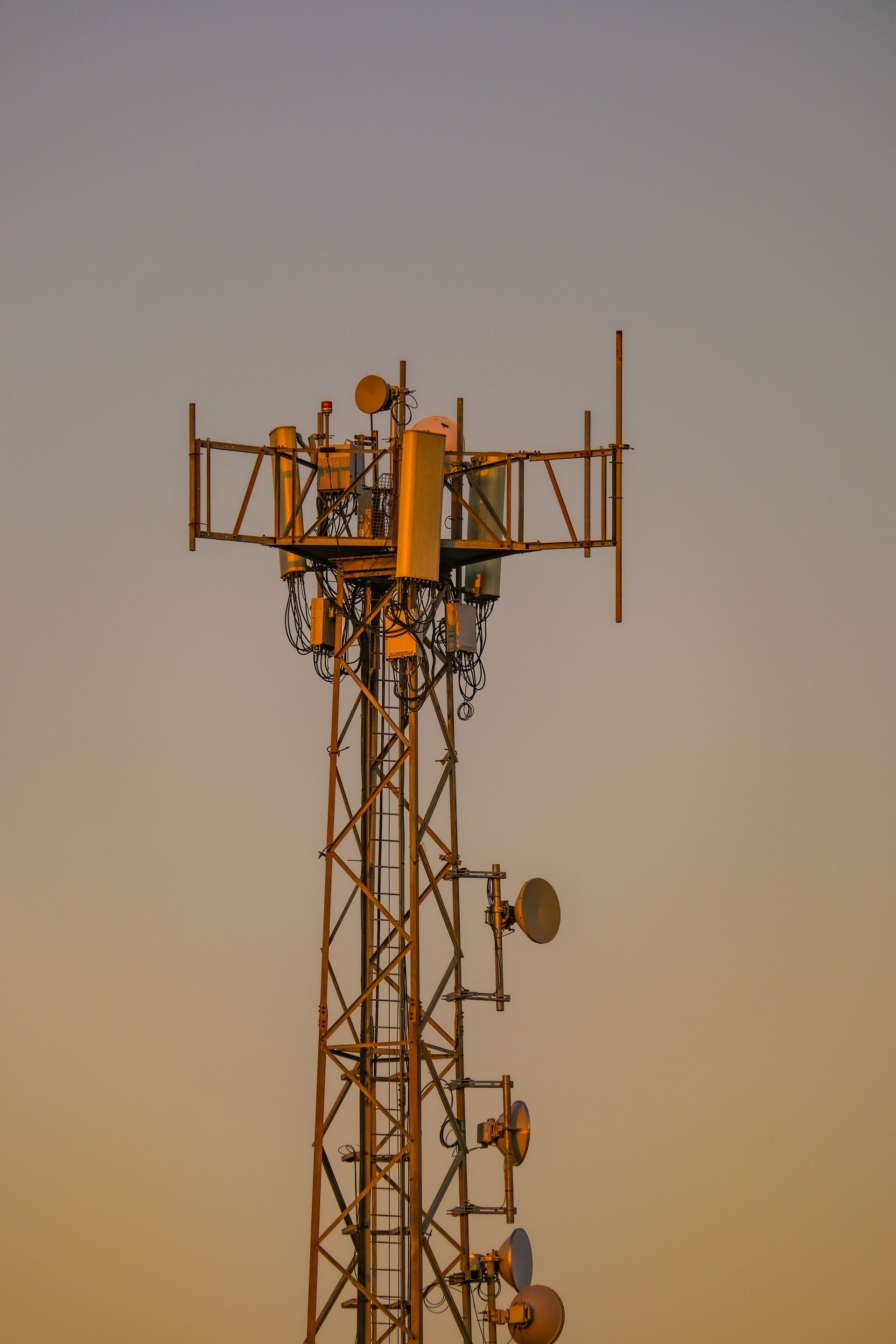 Cell tower with antennas silhouetted against a warm sunset sky