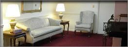 Living room with light sofa, armchair, lamps, and red carpet in a cozy waiting area