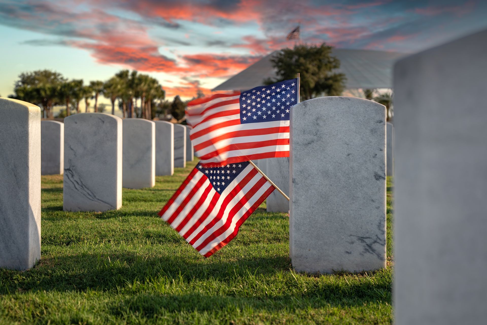 American flags at a cemetery with white gravestones at sunset