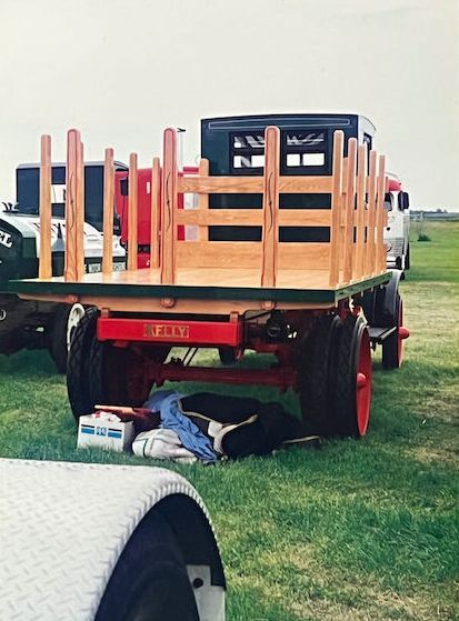 A vintage flatbed truck with a wooden cargo bed and red frame is parked on a grassy field.