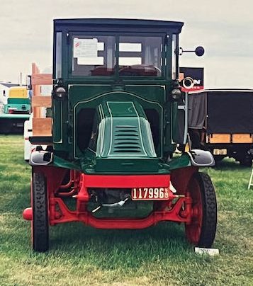 A vintage dark green truck with a red frame parked on grass in an outdoor setting.
