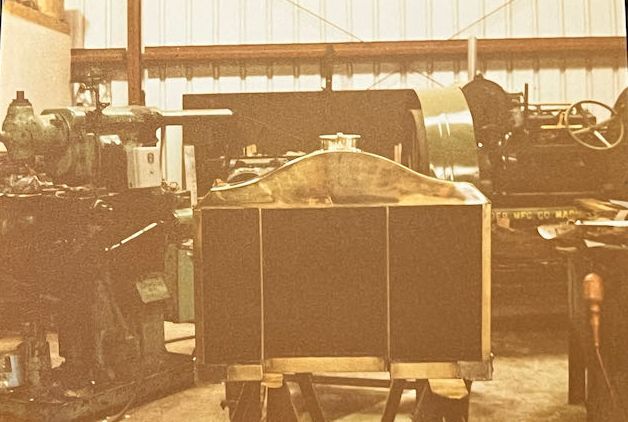 A sepia-toned shop scene showing a large vintage radiator centered in the foreground, flanked by heavy industrial machinery.