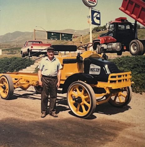 An antique truck with a wooden flatbed, painted red, is parked on a grassy field.