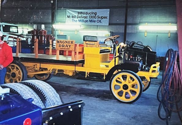 A vintage yellow flatbed truck parked inside a garage, with a sign reading 