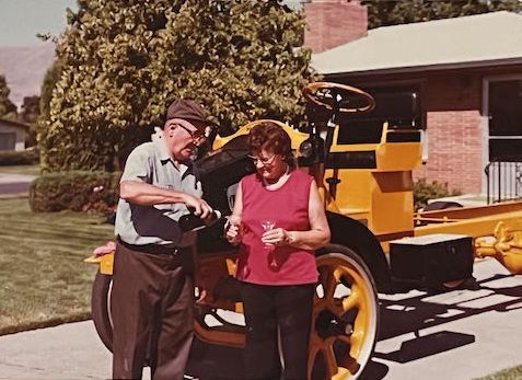 An older couple sits on a vintage yellow truck with a 