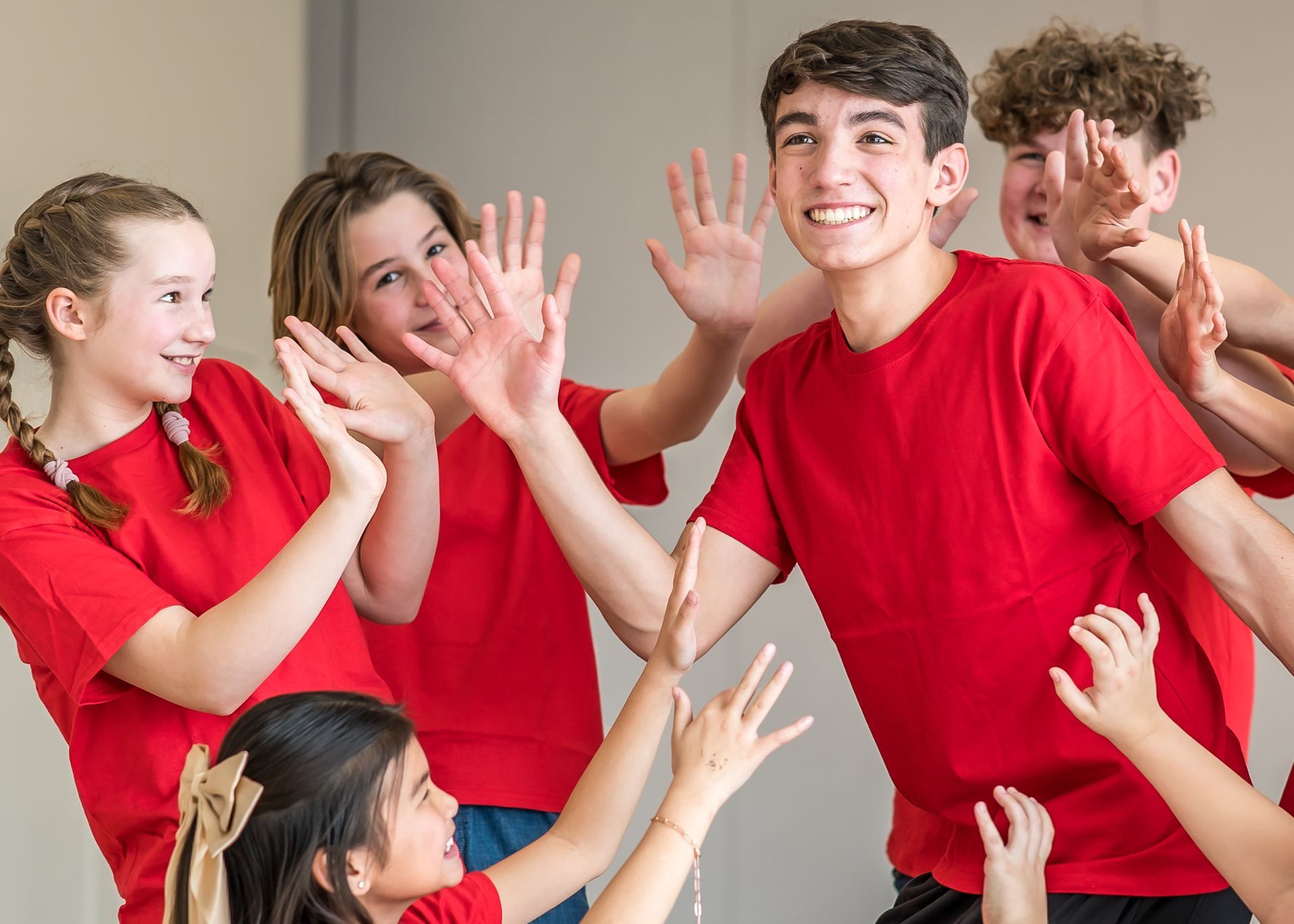 A group of people in matching black t-shirts singing on stage with hands raised, expressions joyous and mouths open.