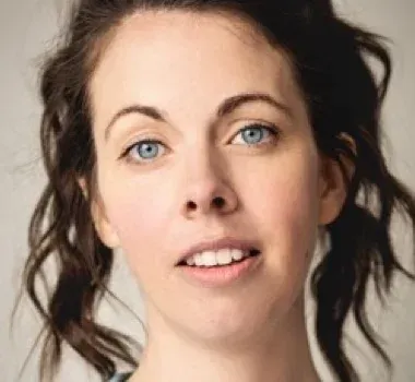 A headshot of a person with wavy brown hair and blue eyes, looking toward the camera with a neutral expression.