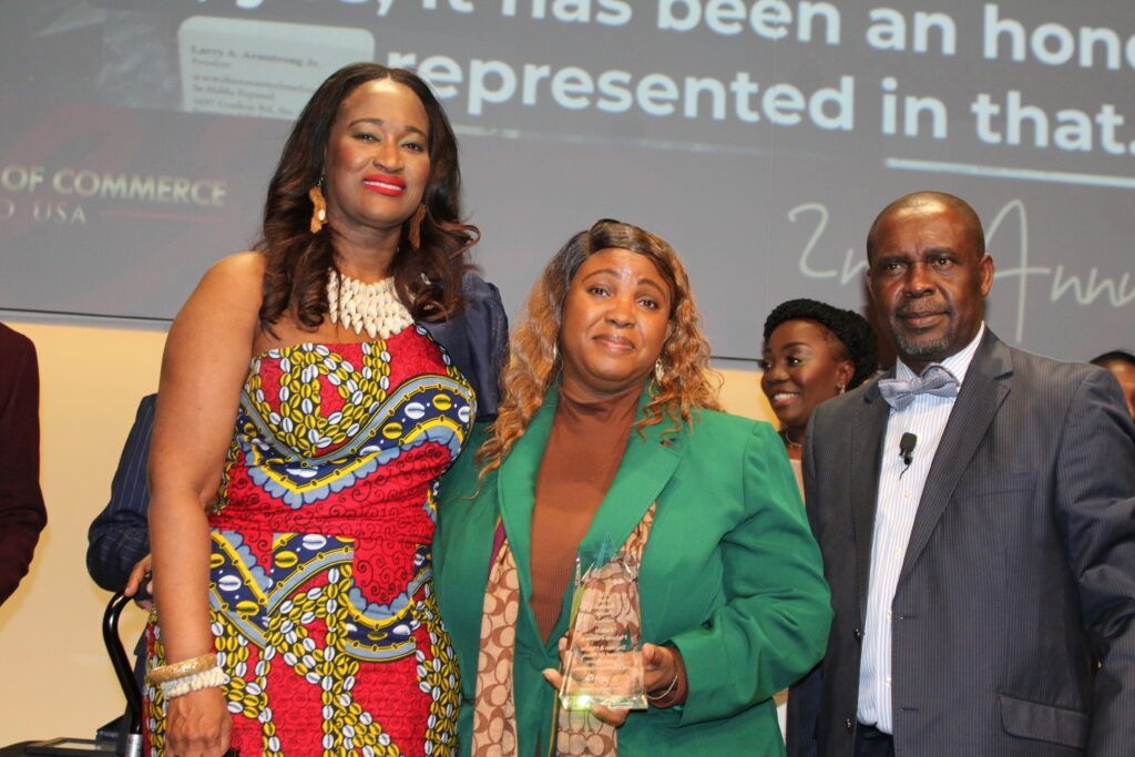 Three people standing onstage at an awards ceremony, posing together and holding a trophy