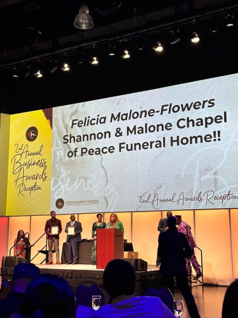 Stage ceremony honoring Felicia Malone-Flowers, with speakers and floral-themed backdrop at Peace Funeral Home