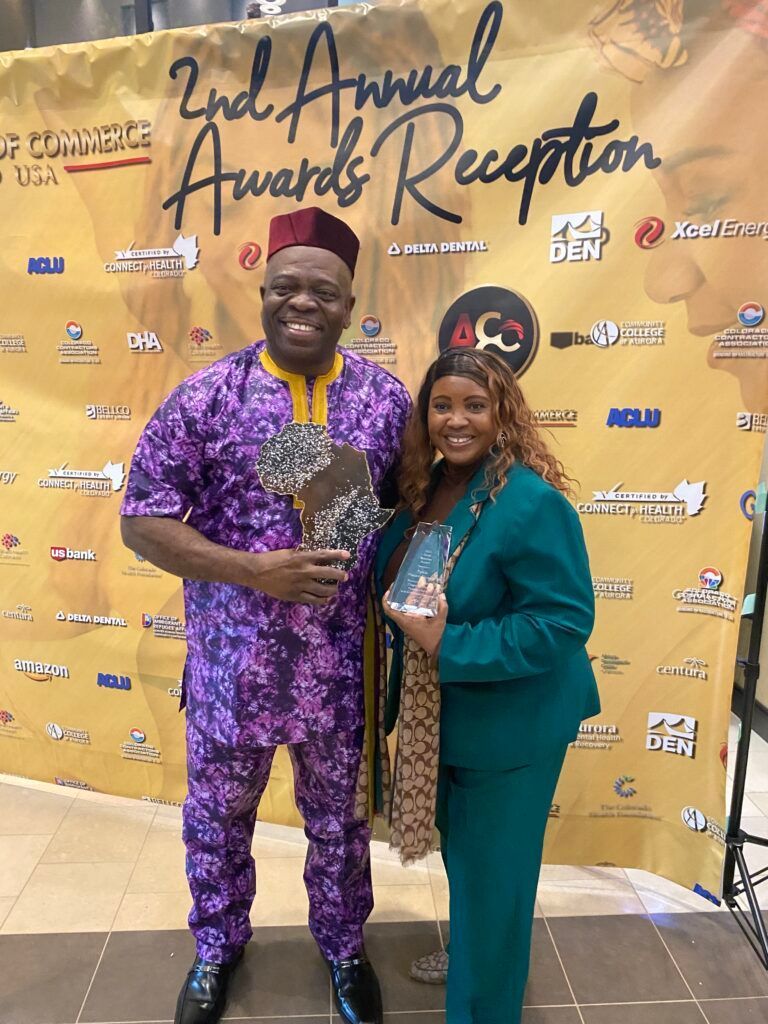 Two people smiling at an awards reception, holding a trophy in front of a step-and-repeat backdrop.