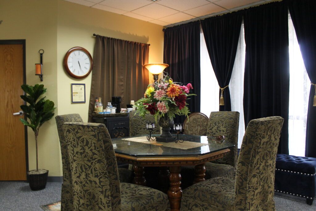 Conference room with round table, patterned chairs, flowers, lamp, clock, and curtained windows