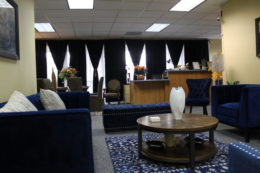 Modern lobby with blue couches, round coffee table, and a reception desk under bright ceiling lights.