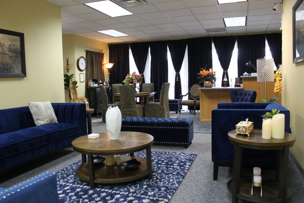 Office lounge with blue sofas, coffee tables, and patterned rugs in front of a curtained window.