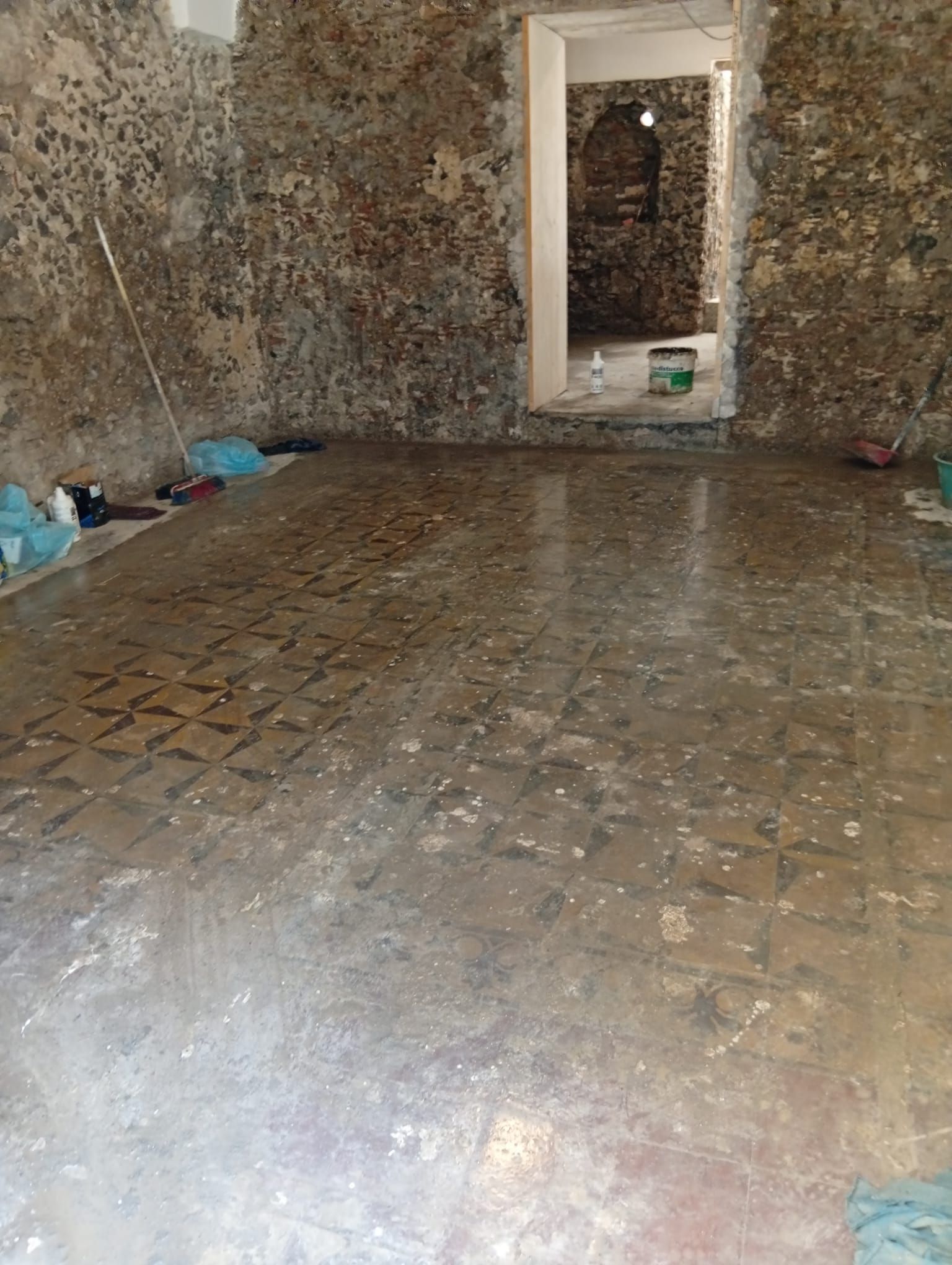Stanza con pareti in pietra, pavimento piastrellato bagnato e porta aperta su un'altra stanza.