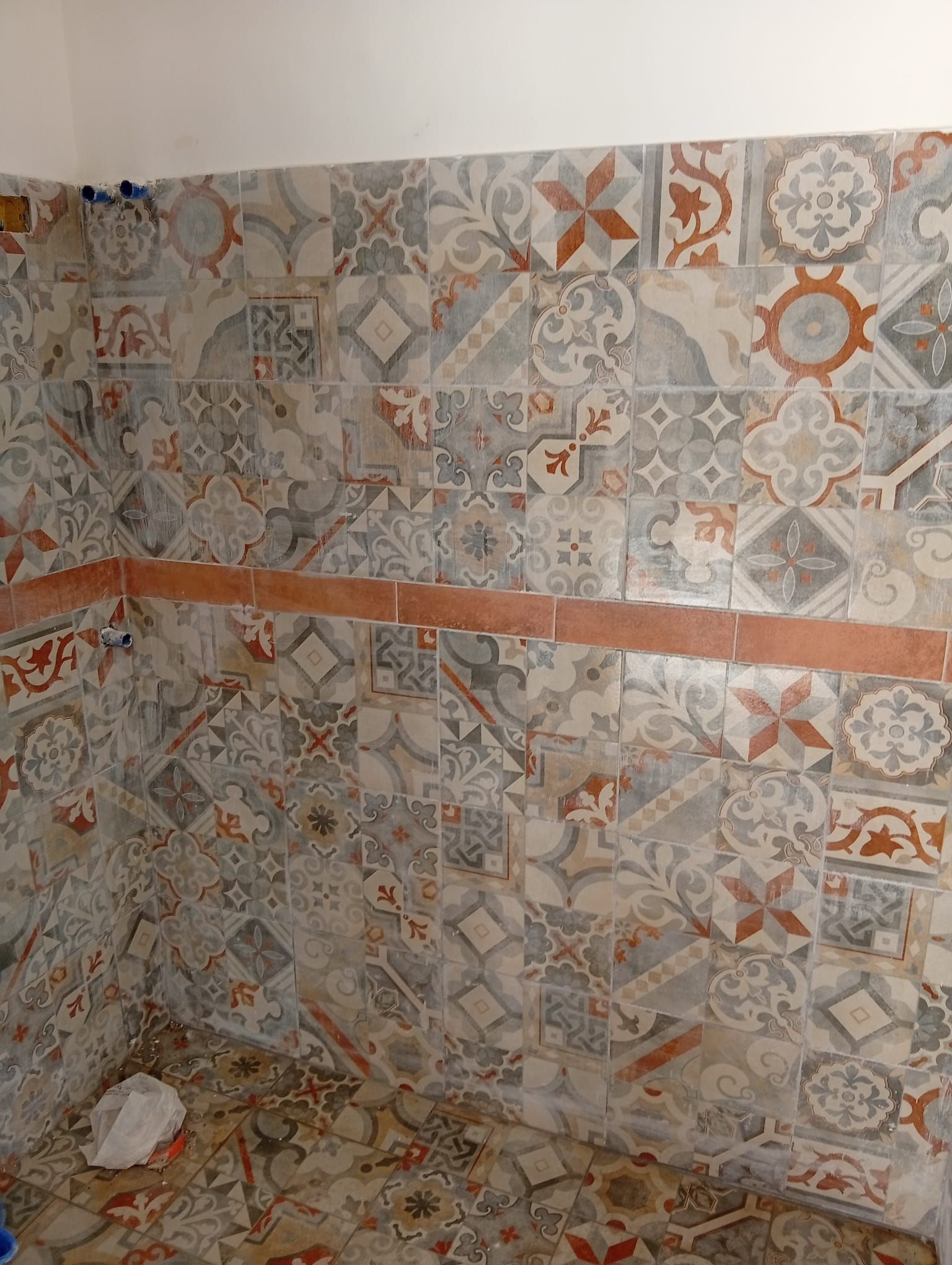 Parete della doccia rivestita con piastrelle decorate nei toni del grigio, bianco e arancione e una striscia decorativa orizzontale arancione.