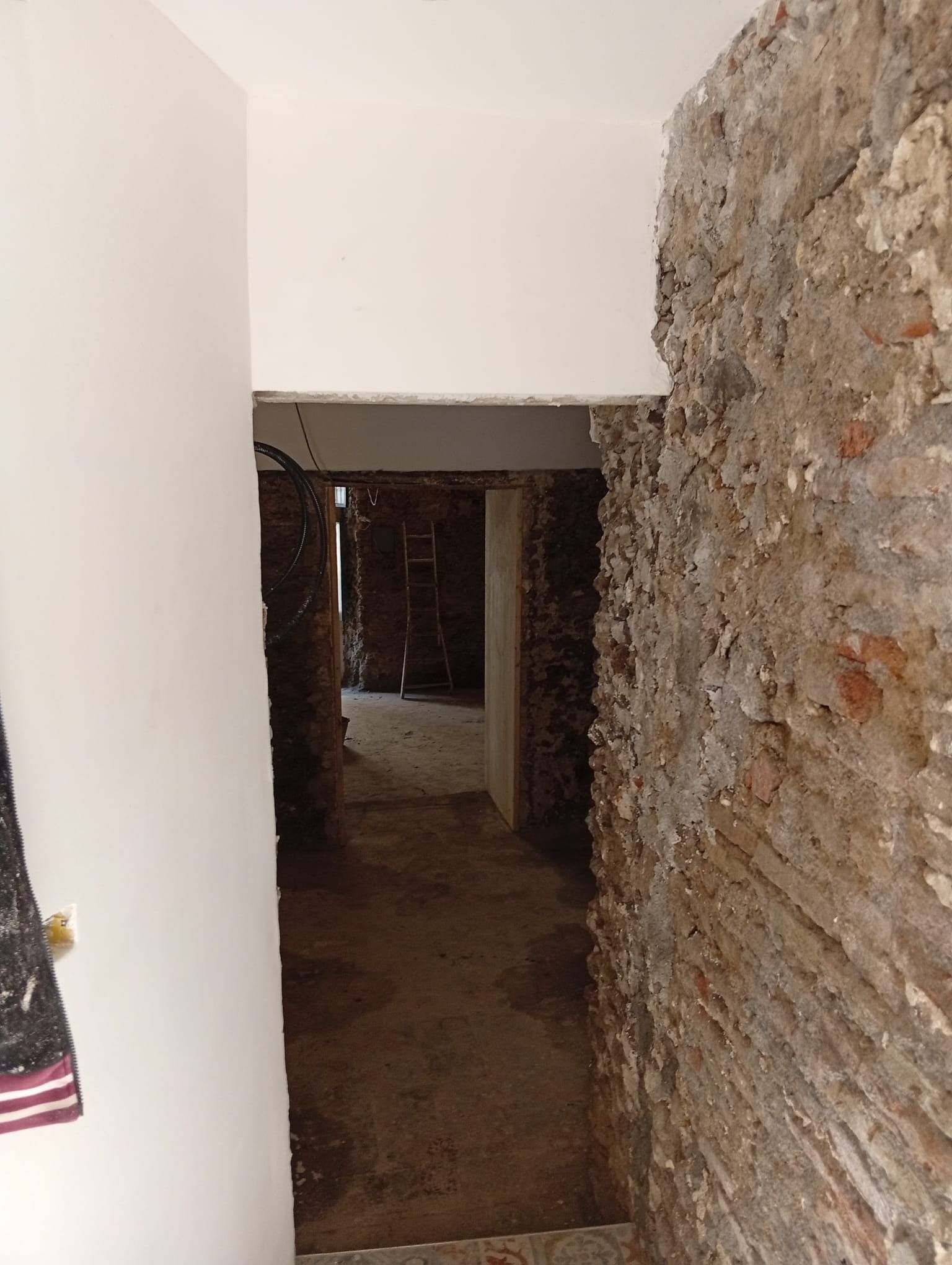 Stretto corridoio in pietra con una parete bianca, che conduce a un passaggio interno più scuro.