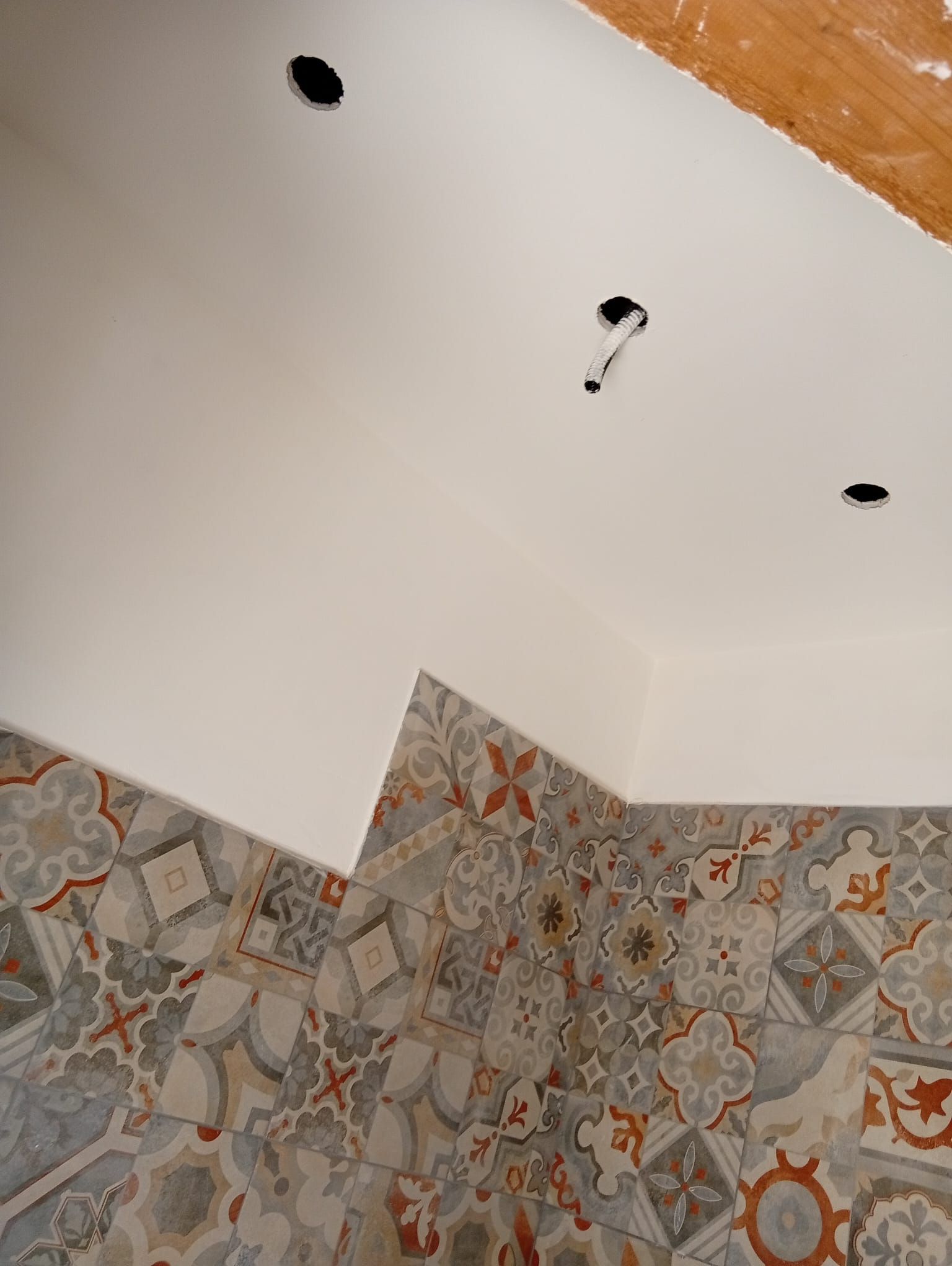 Parete e soffitto del bagno piastrellati, con fori a vista per i punti luce e vernice bianca.