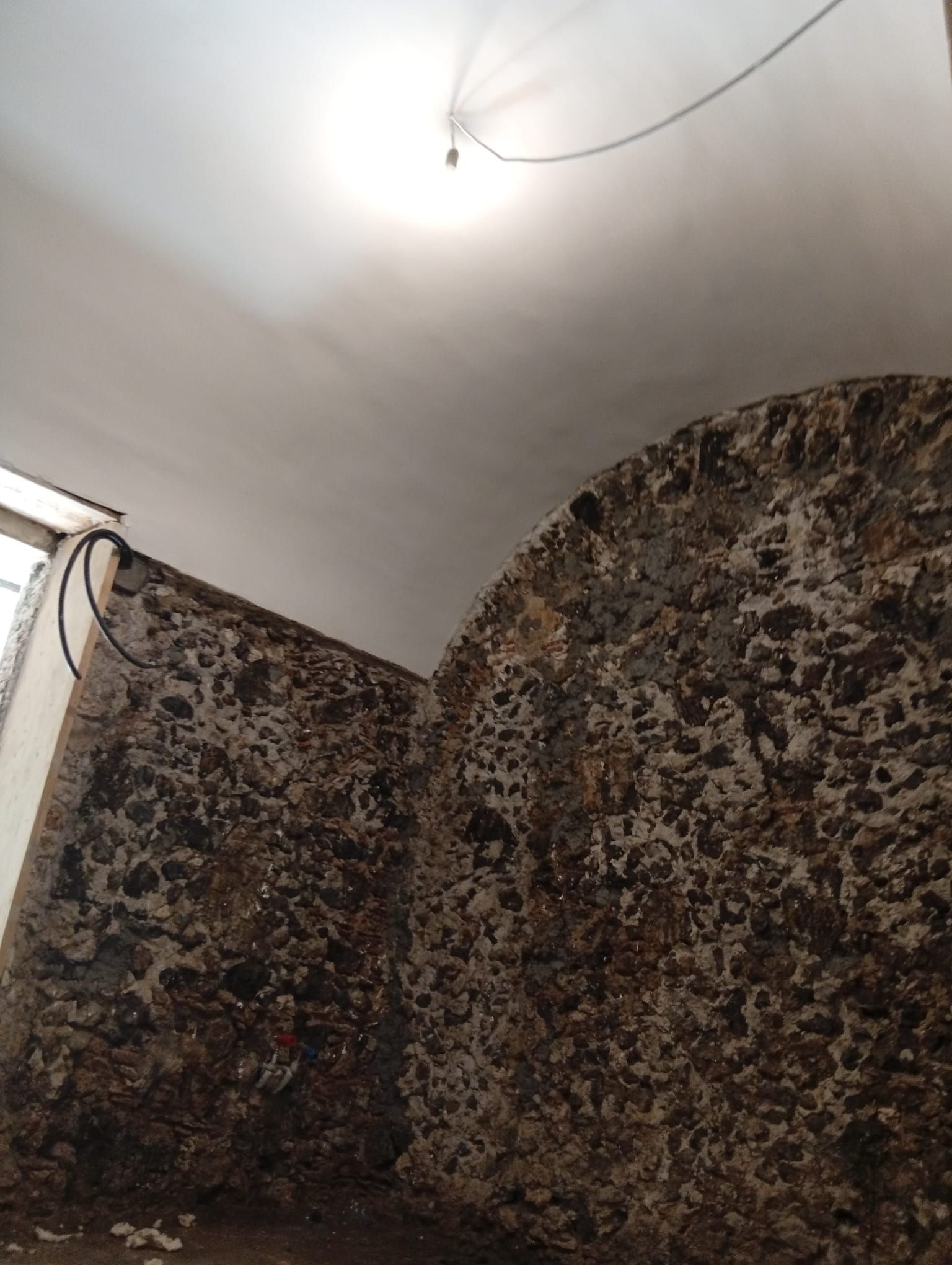 Stanza in penombra con carta da parati a motivi floreali e una lampadina nuda su un soffitto bianco e curvo.