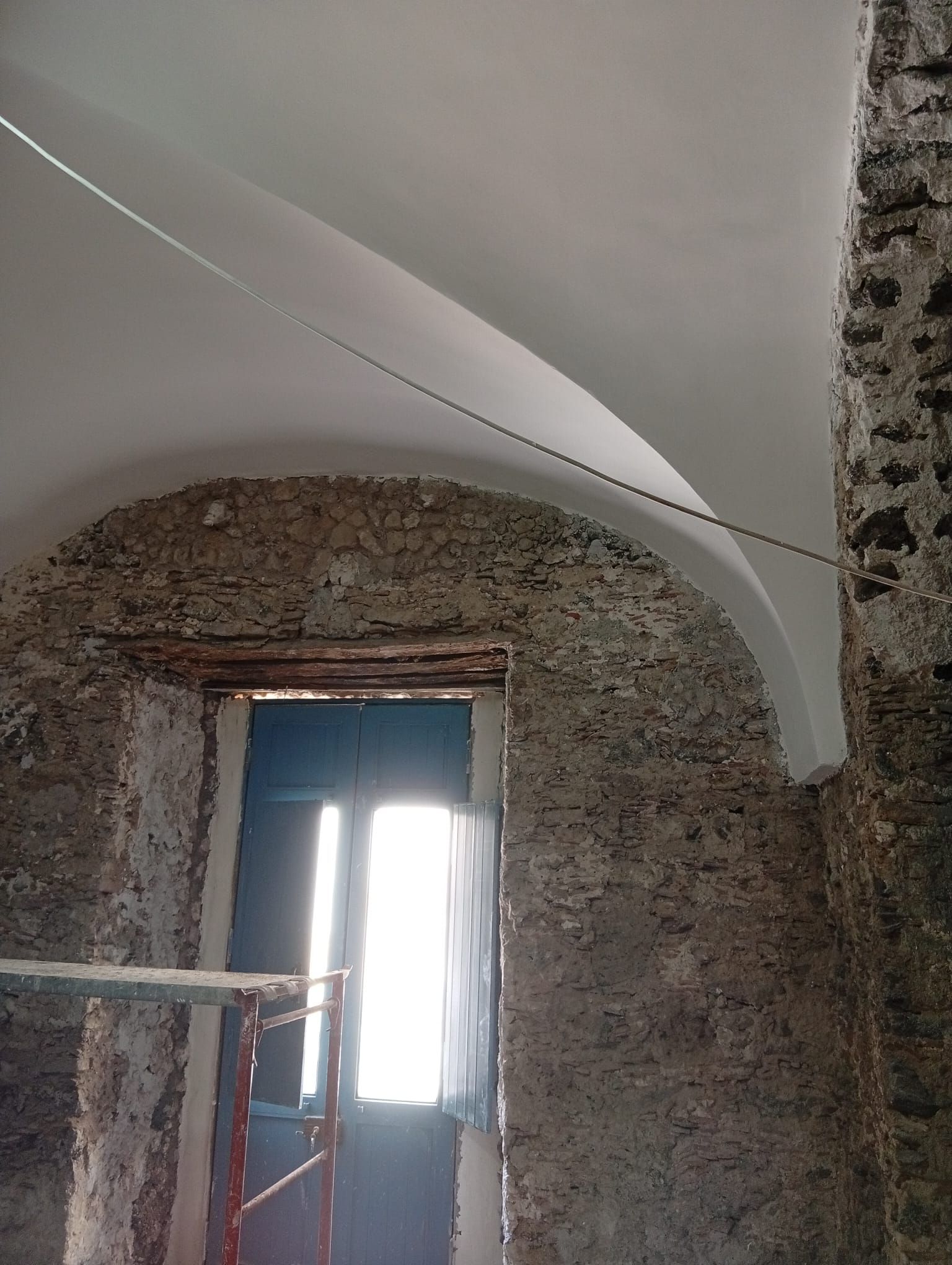 Camera in pietra parzialmente ristrutturata con soffitto a volta e luminosa porta al centro.