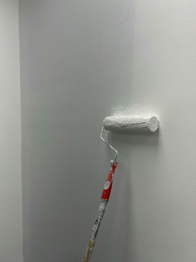 Rullo da pittura su una parete grigia, con applicazione di vernice bianca in una striscia orizzontale.