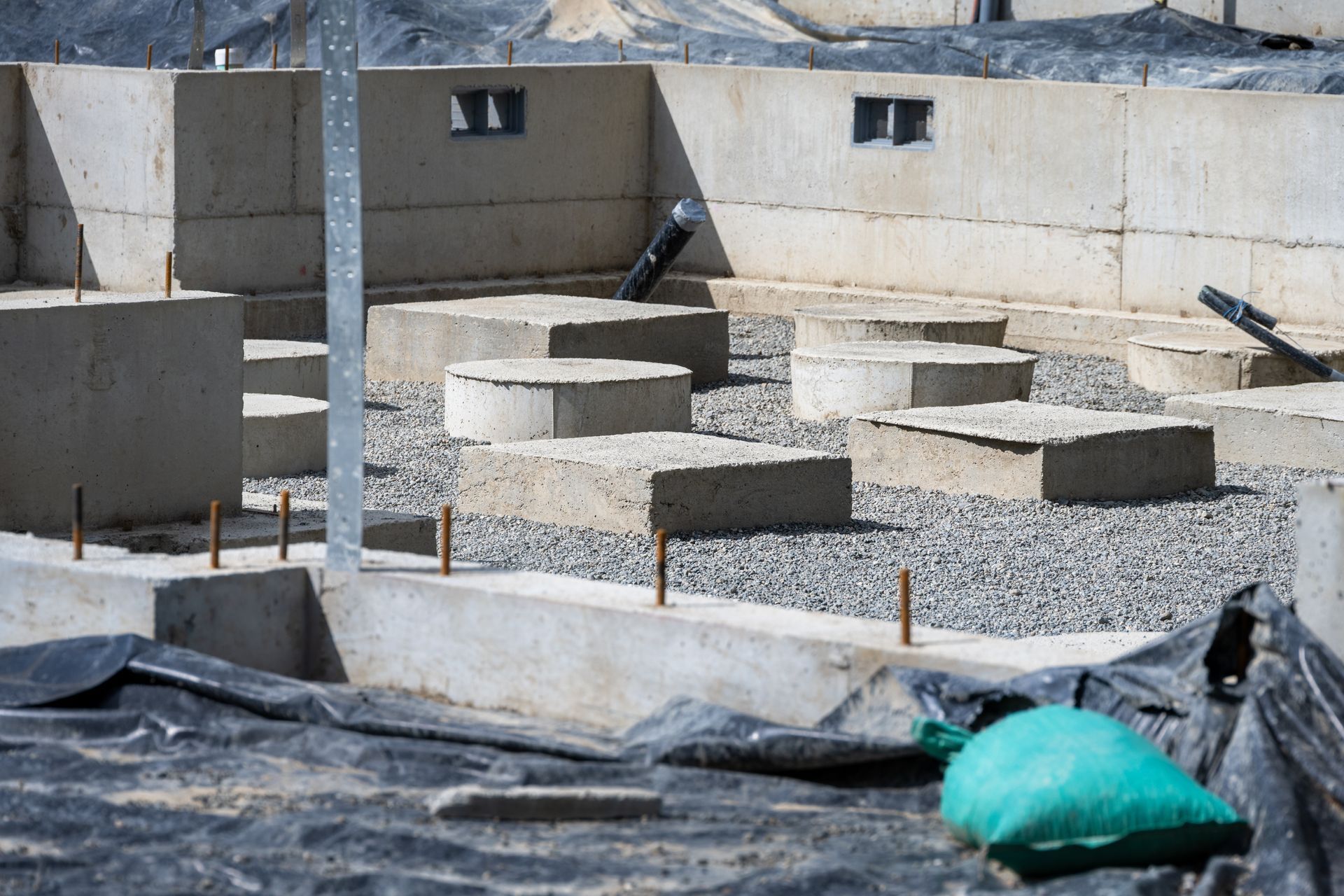 Concrete foundation with several round footings and black tarp in a construction site