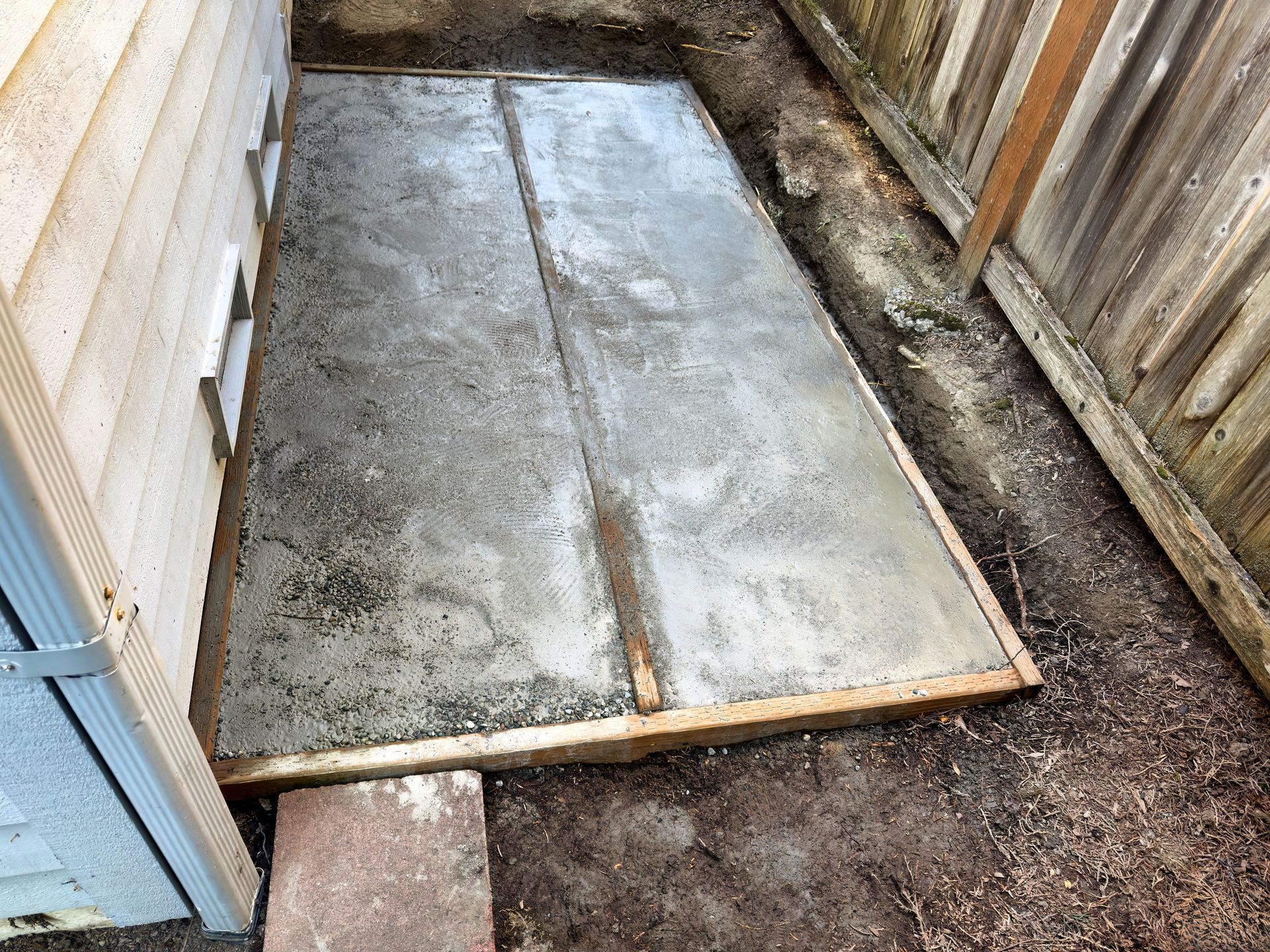 Wooden ramp over a muddy, narrow passage beside weathered siding and a fence