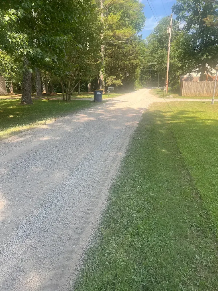 Gravel driveway lined with trees and grass, curving into the distance on a sunny day