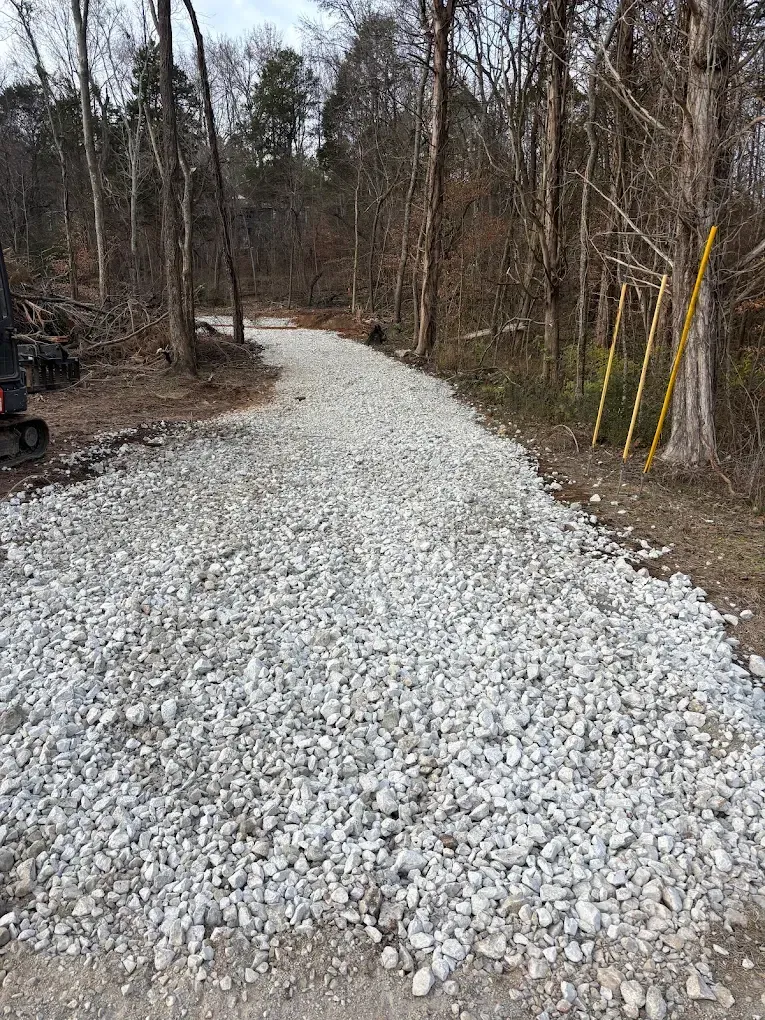 Gravel driveway curving through a wooded area with leafless trees and yellow stakes on the right