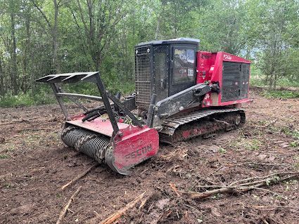 Skid steer with brush cutter clearing a dirt path in a wooded area.