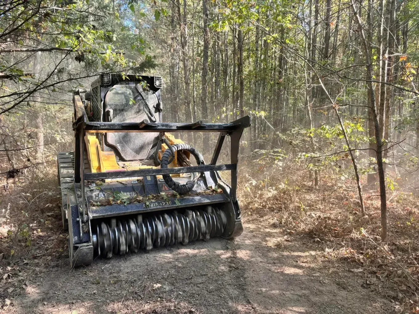 Yellow forestry machine clearing leaves on a wooded dirt path
