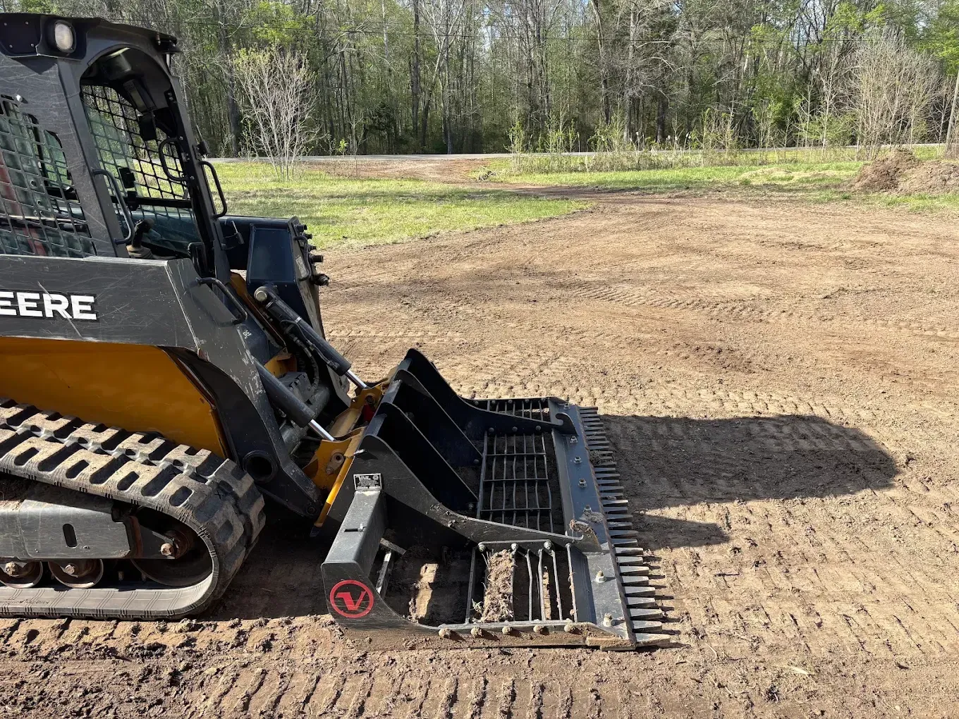 Black skid-steer loader with grapple bucket on a dirt field near a tree line