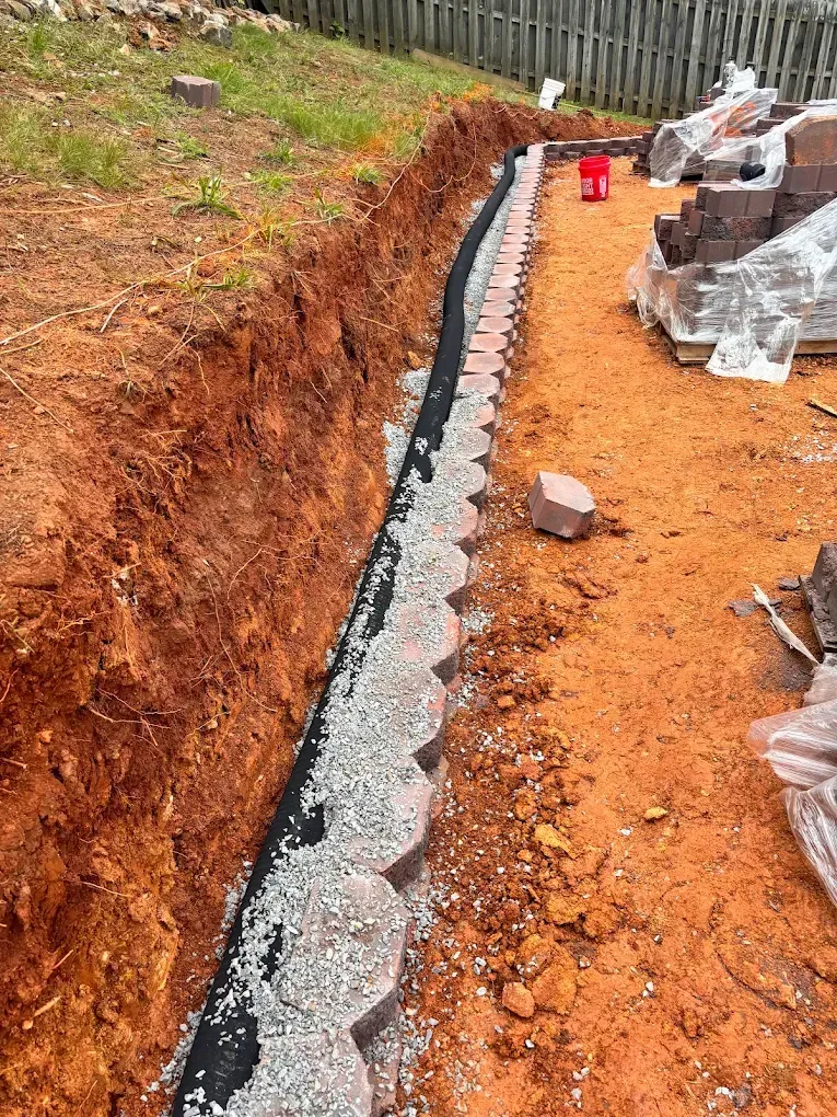 Trenched ditch lined with gray gravel beside red dirt and construction materials outdoors