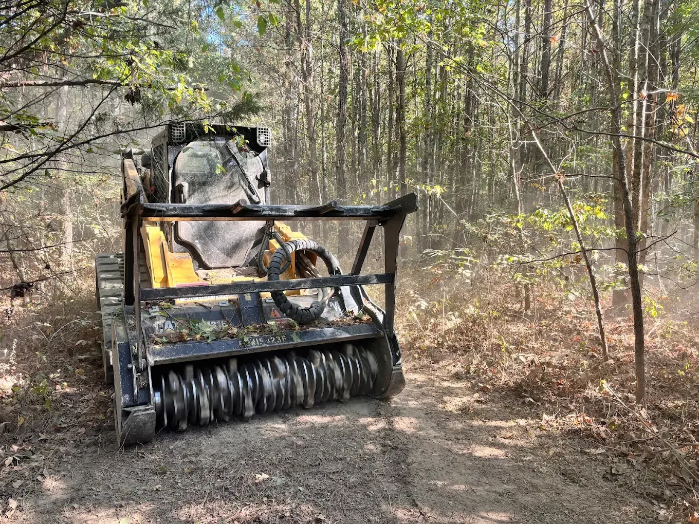 Yellow brush cutter clearing a forest trail in a wooded area