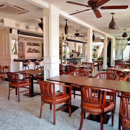 A restaurant interior with tables, chairs, a bar, ceiling fans, and large windows.