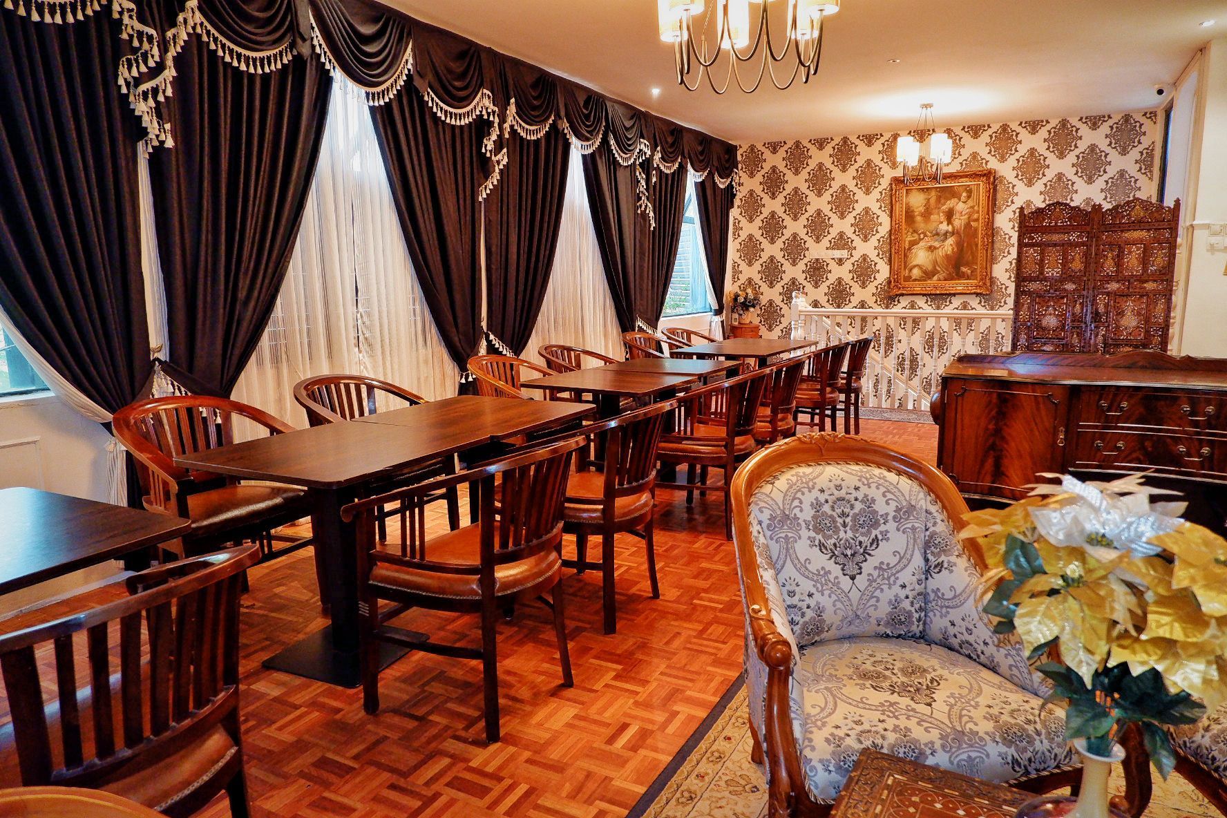 Restaurant interior with dark curtains, wood tables and chairs, and ornate wallpaper.