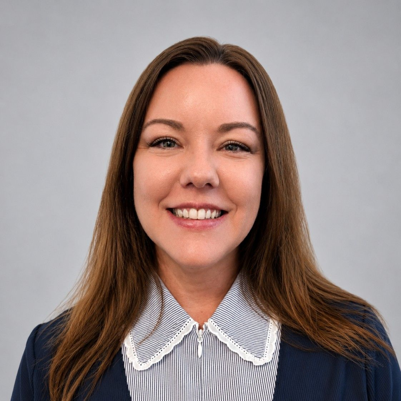 Smiling woman in a navy top and white collared blouse against a gray background