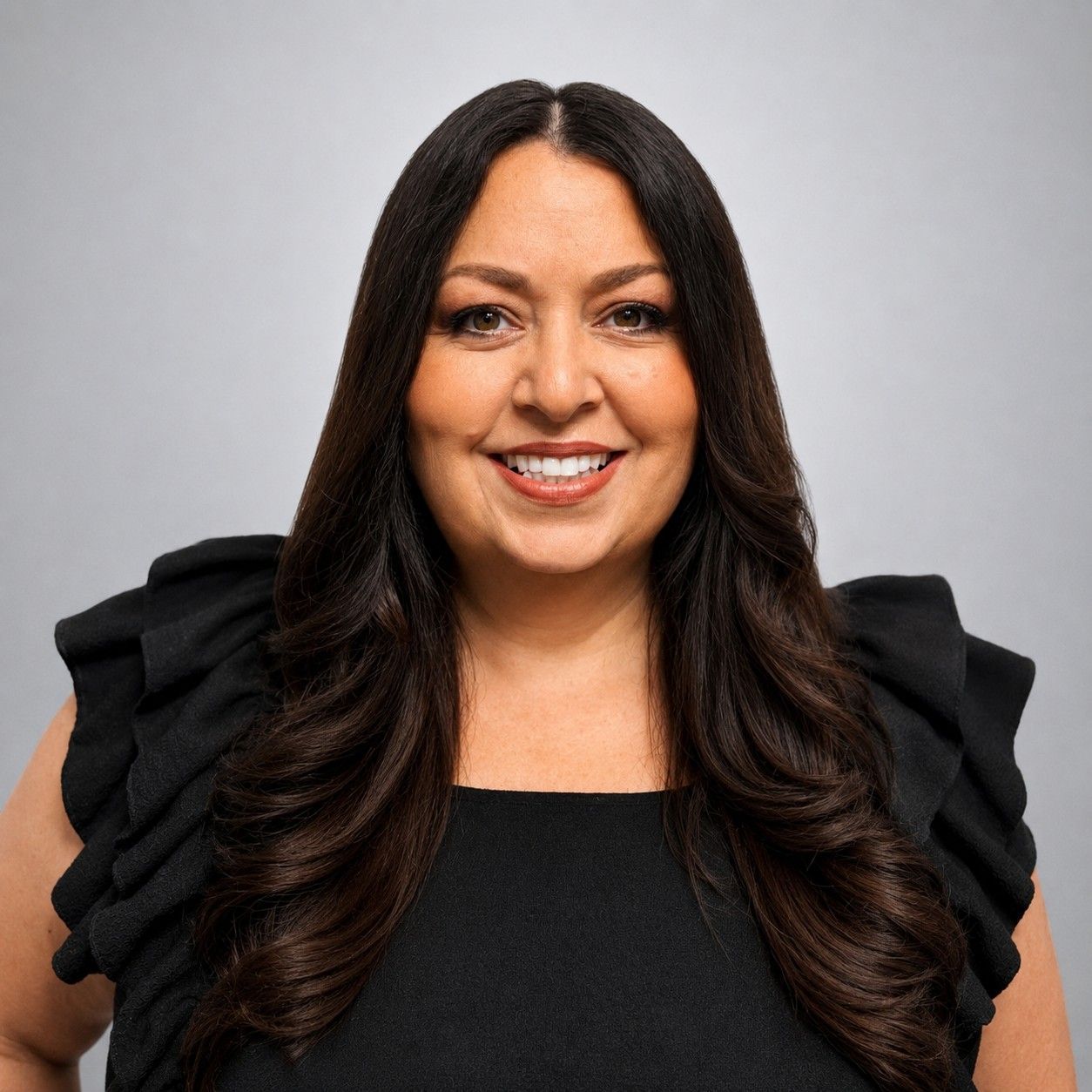 Smiling woman with long dark hair wearing a black dress against a light gray background