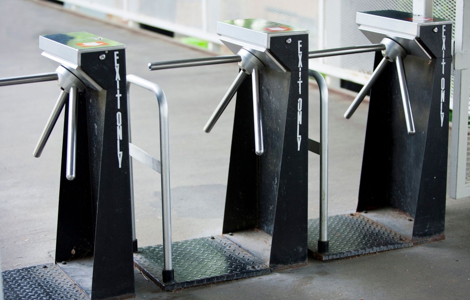 Three black turnstiles with silver arms, likely at an entrance or exit.