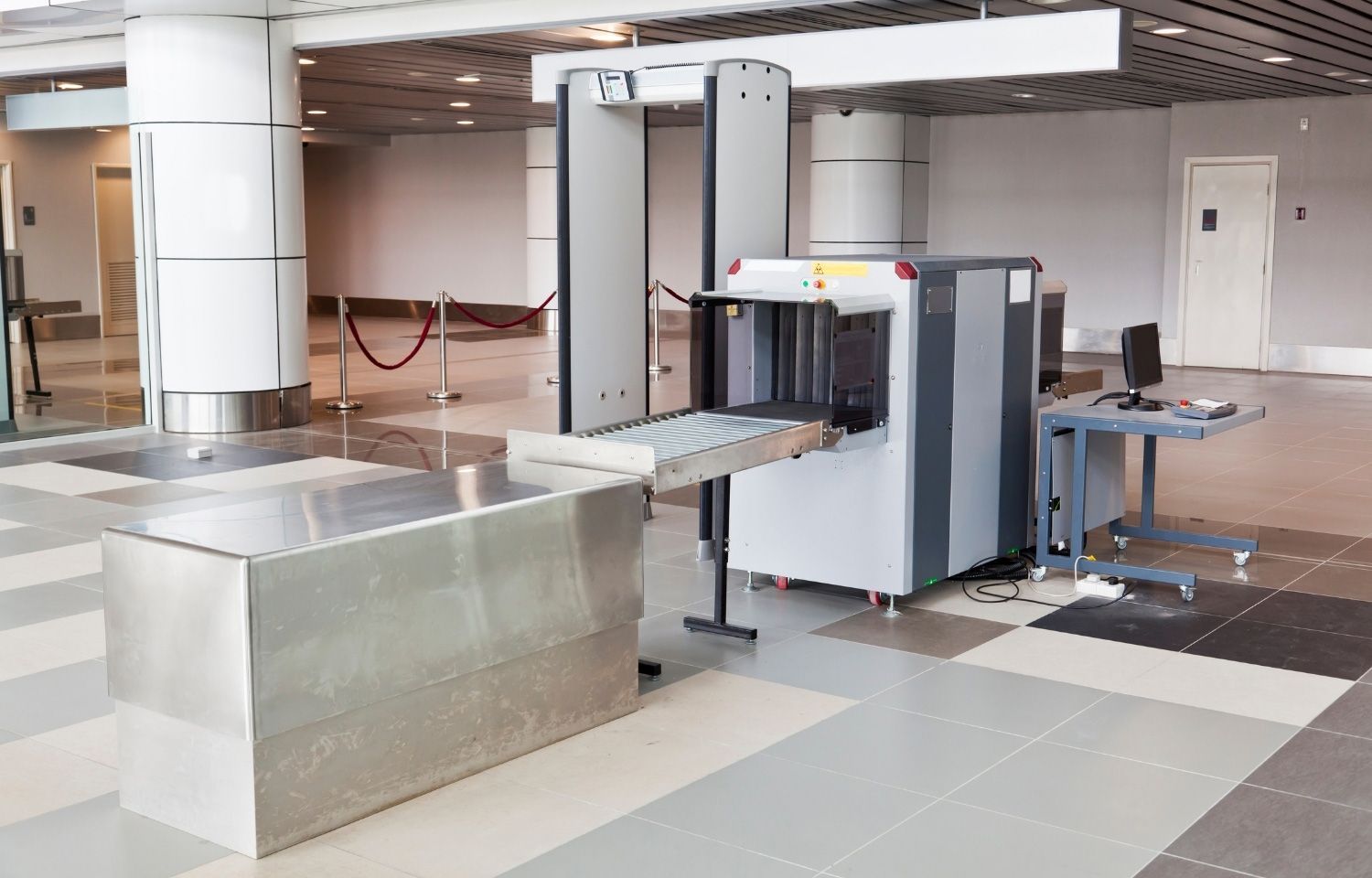Security checkpoint with baggage scanner, metal detector, and conveyor belt, in a brightly lit building.