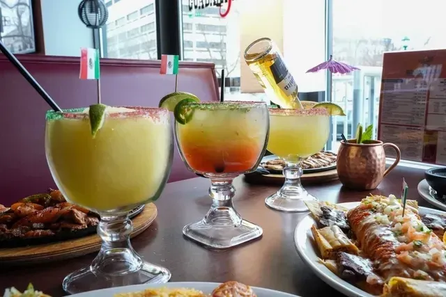 Three margaritas on a table with food, including a Corona bottle upside down in one.