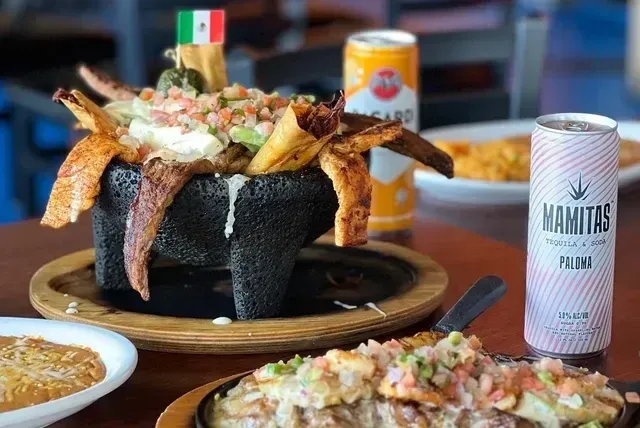 A table with a molcajete overflowing with nachos, drinks, and other Mexican dishes.