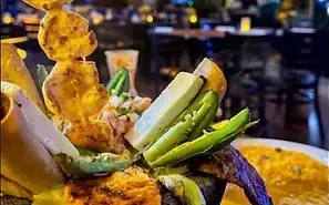Close-up of a loaded dish with grilled items, jalapeños, and cheese sticks. Restaurant setting with dimly lit background.